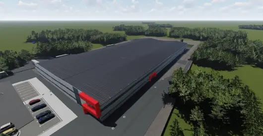 A large, modern industrial warehouse with a grey and red exterior, surrounded by a green landscape and dense trees under a partly cloudy sky.